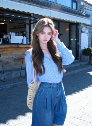 young woman posing on a sunny street wearing striped blouse and denim shorts